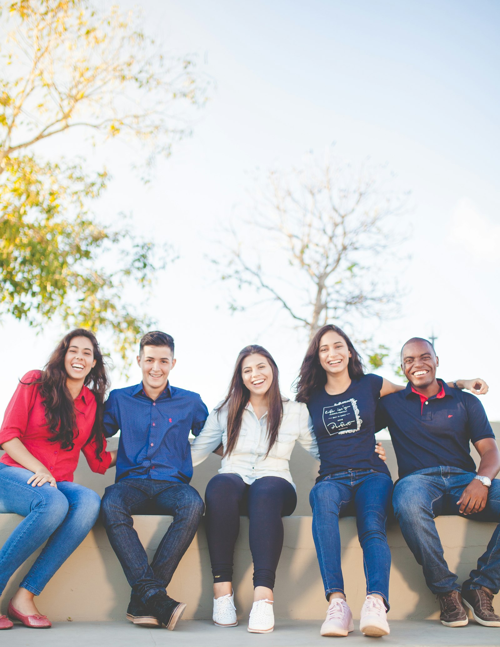 Five friends sitting shoulder to shoulder, laughing together in the sunshine